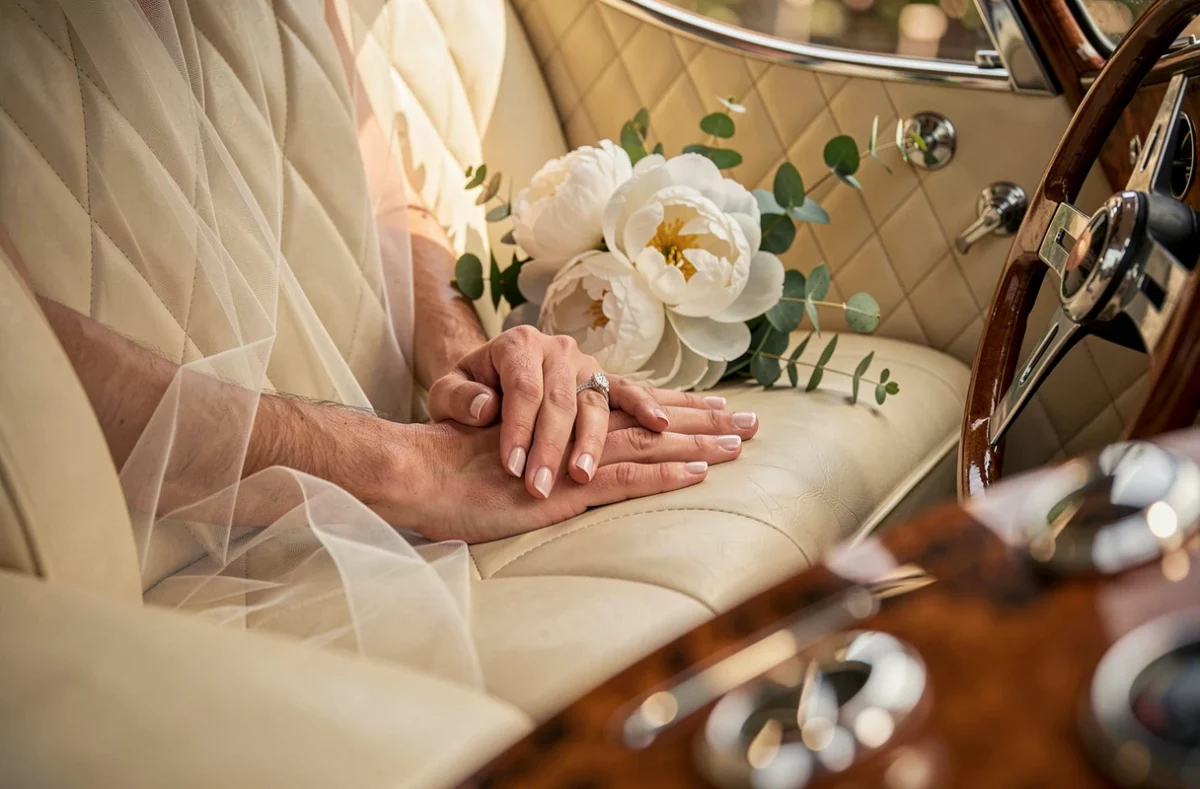 Intérieur en cuir crème d'une Bentley vintage de mariage à Toulouse avec mains de mariés et bouquet de pivoines blanches